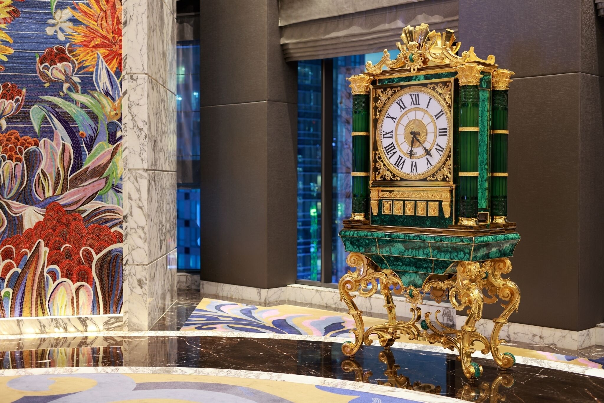 A grand clock with Roman numerals, set on a marble floor with a colorful mosaic backdrop.