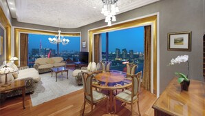 A spacious living room with a round glass table, comfortable seating, a chandelier, and a city view through large windows. - The Reverie Saigon Residential Suites (Ho Chi Minh City)