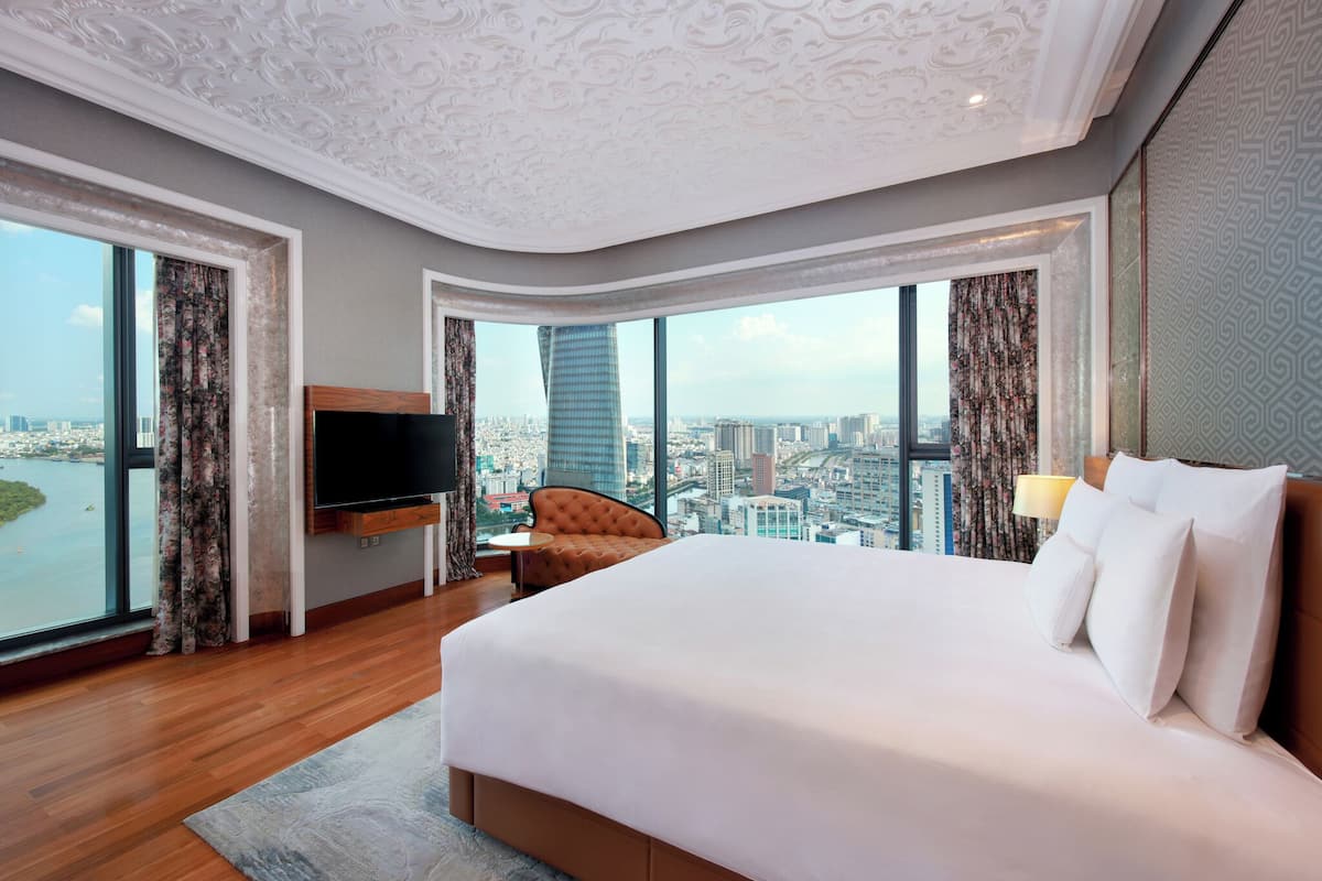 A hotel room with a large bed, a TV, a chair, and a view of a cityscape.