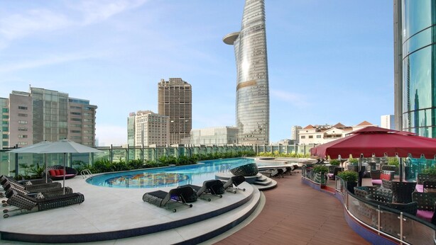 A rooftop pool area with lounge chairs and umbrellas, surrounded by modern buildings and a clear sky. - The Reverie Saigon Residential Suites (Ho Chi Minh City)