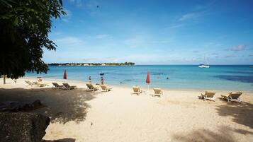 Une plage avec des chaises longues et des parasols, un ciel bleu dégagé et une mer calme.