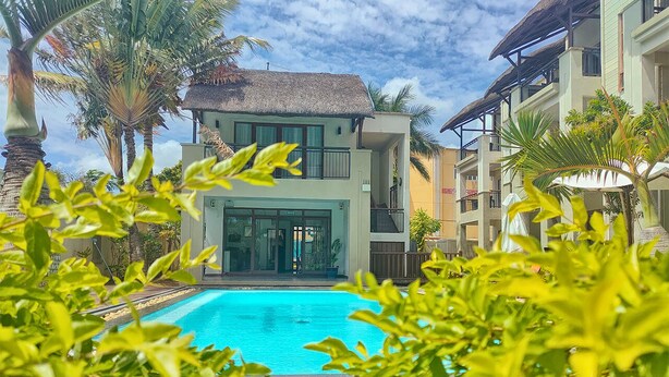 A hotel with a swimming pool, surrounded by lush greenery and palm trees. - Grand Bay Suites (Grand-Baie)