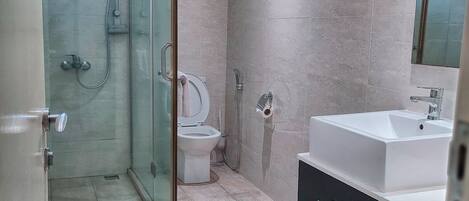 A bathroom with a glass-enclosed shower, a toilet, and a sink with a mirror.