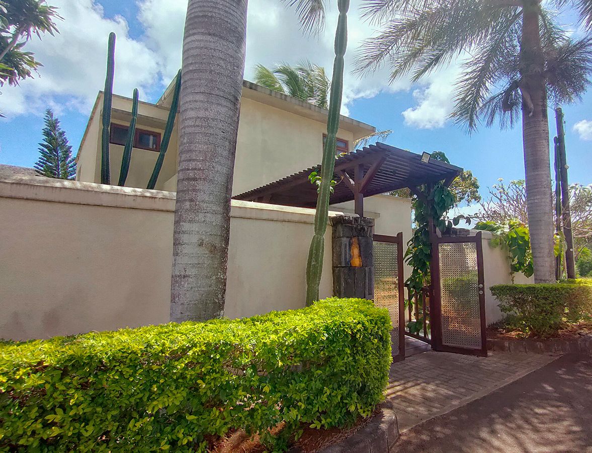 A gated entrance with a palm tree and a building with a flat roof.