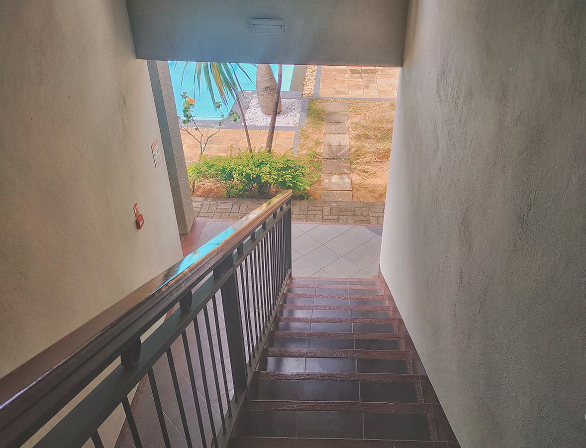 A staircase with a metal railing leading to an outdoor area with a pool and palm trees.