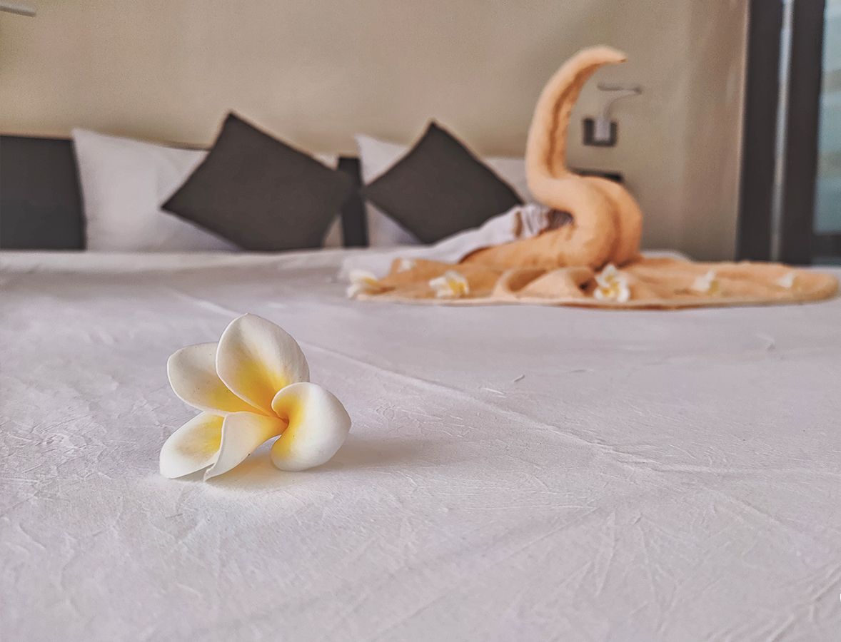 Una cama con una colcha blanca, un cojín decorativo con forma de cisne y una flor blanca.