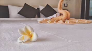 Una cama con una colcha blanca, un cojín decorativo con forma de cisne y una flor blanca.