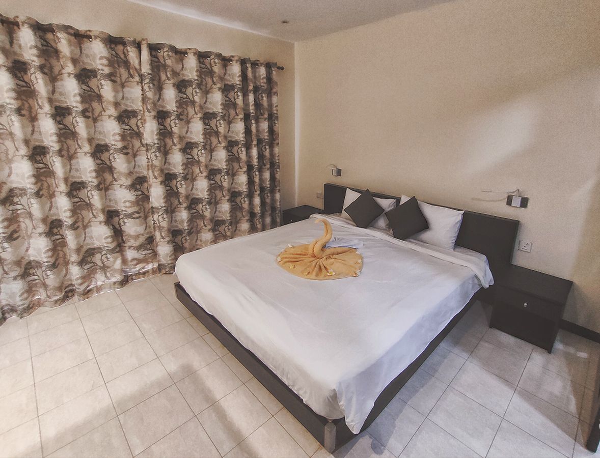 A hotel room with a bed, a nightstand, a wall-mounted lamp, and a curtain with a leaf pattern.
