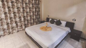 A hotel room with a bed, a nightstand, a wall-mounted lamp, and a curtain with a leaf pattern.
