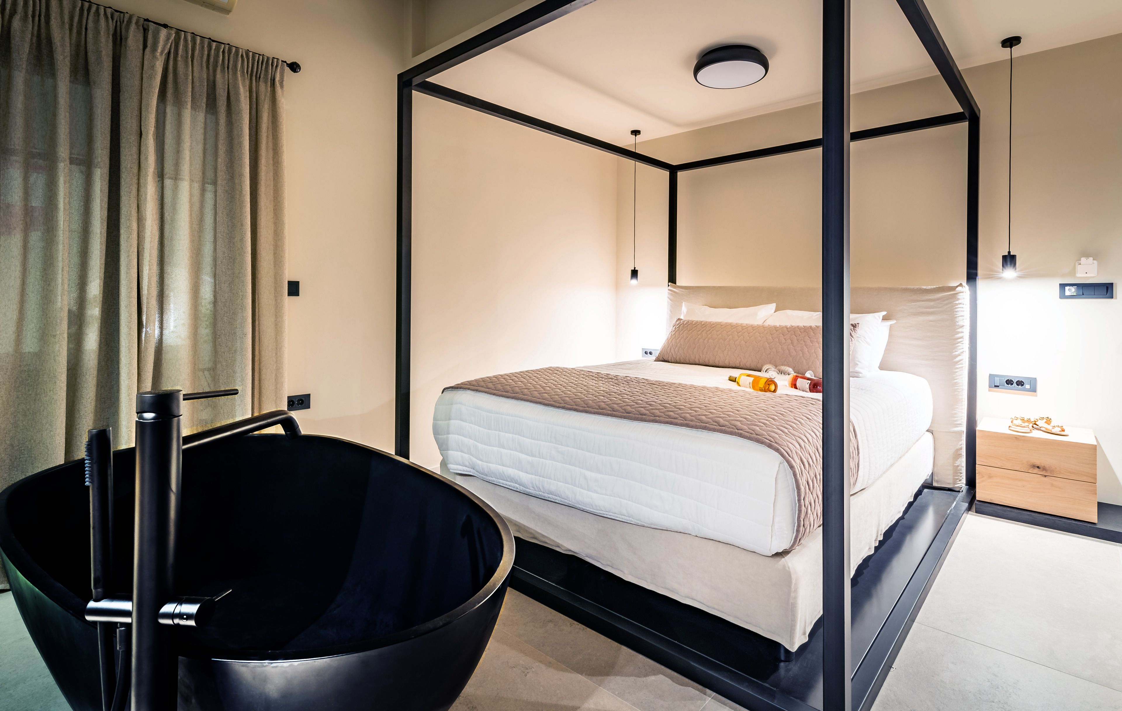 Ein modernes Hotelzimmer mit einem Himmelbett, einer schwarzen Badewanne und einem Nachttisch mit Lampe.