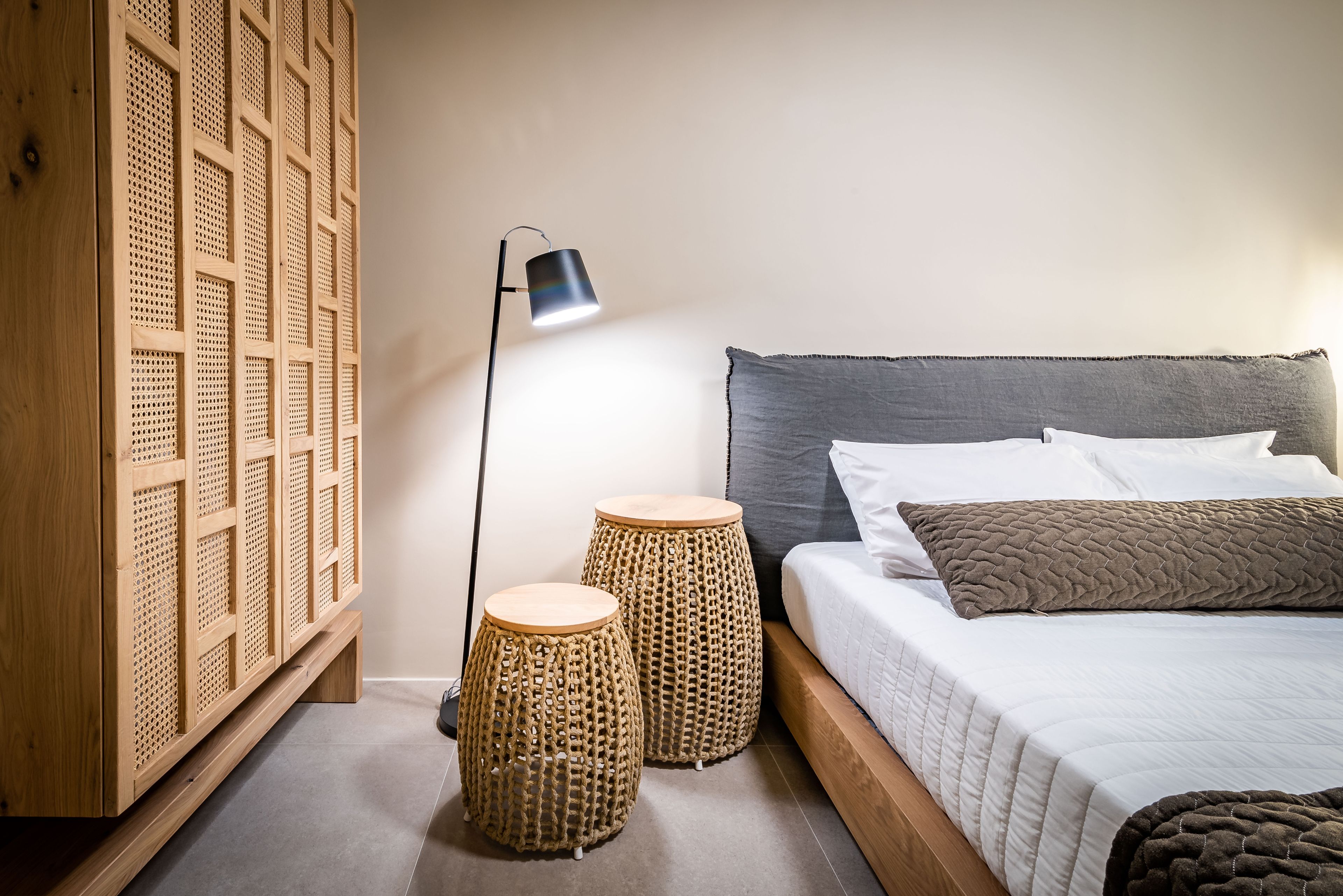 Une chambre à coucher avec un lit, une lampe de chevet et deux tabourets en osier.