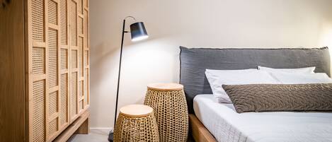 Un dormitorio con una cama, una lámpara de noche y dos taburetes de mimbre.