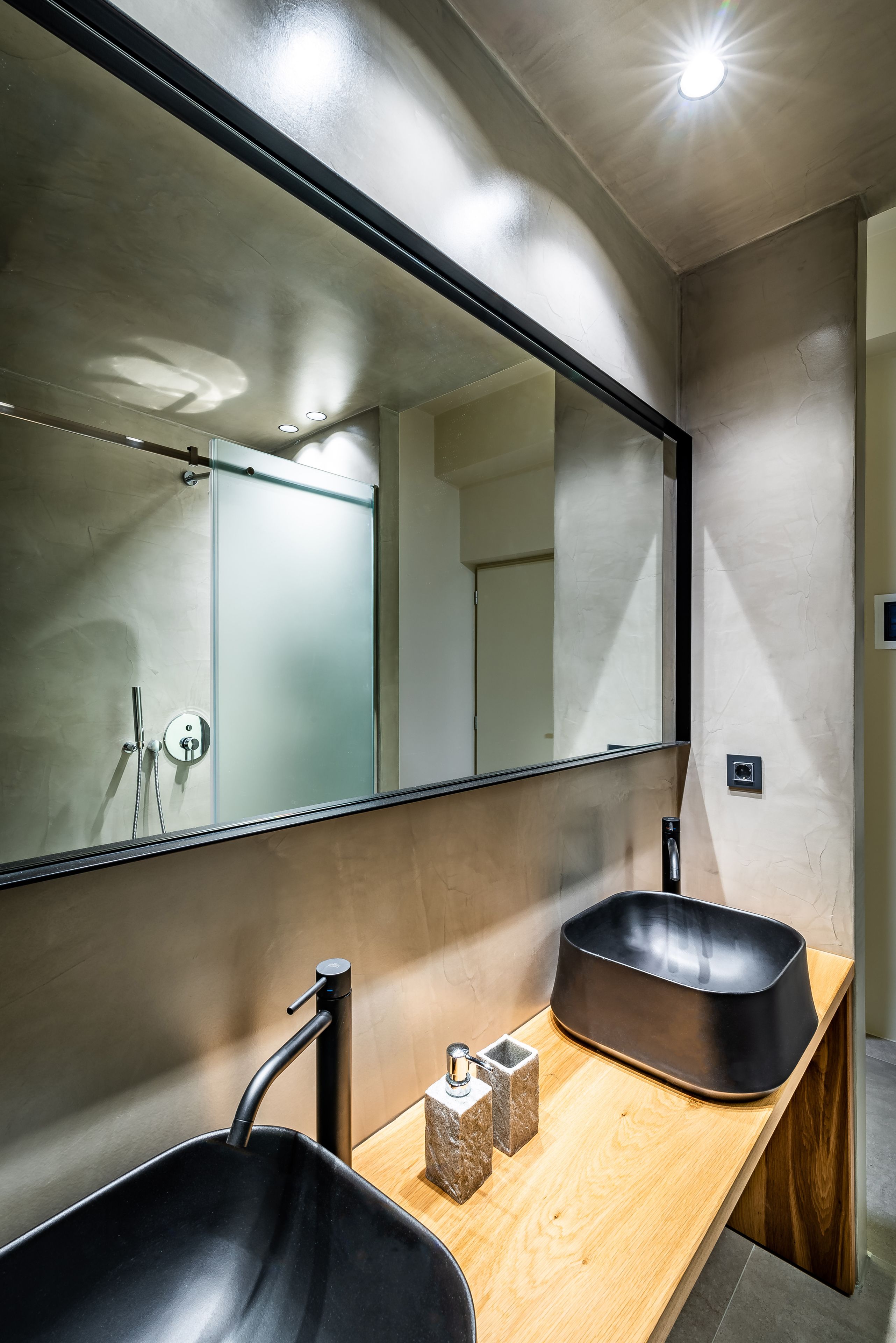 Une salle de bain moderne avec un grand miroir, un lavabo noir et un plan de toilette en bois.