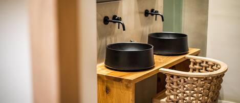 A bathroom with two black sinks on a wooden countertop, a wooden chair, and a mirror above the sinks.