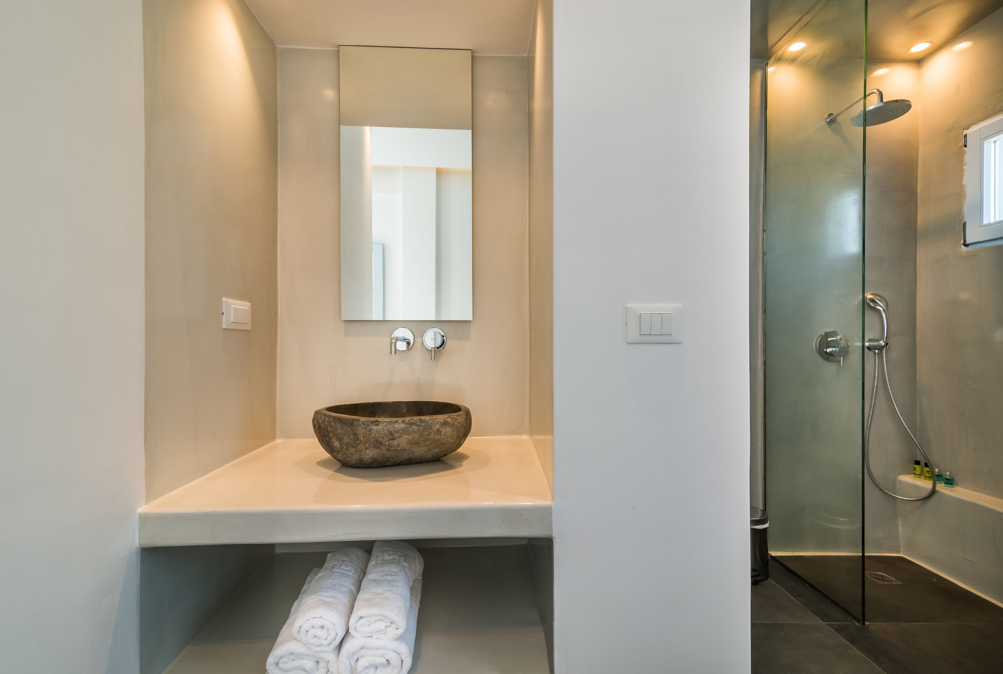 A modern bathroom with a large mirror, a bowl sink, and a glass-enclosed shower.