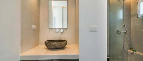 A modern bathroom with a large mirror, a bowl sink, and a glass-enclosed shower.
