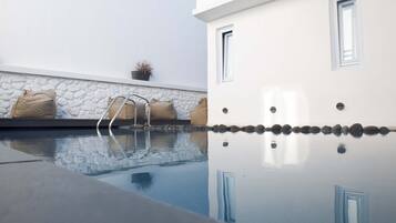 Uma área de piscina moderna com vista clara da borda da piscina, uma escada e um muro de pedra com um vaso de planta.