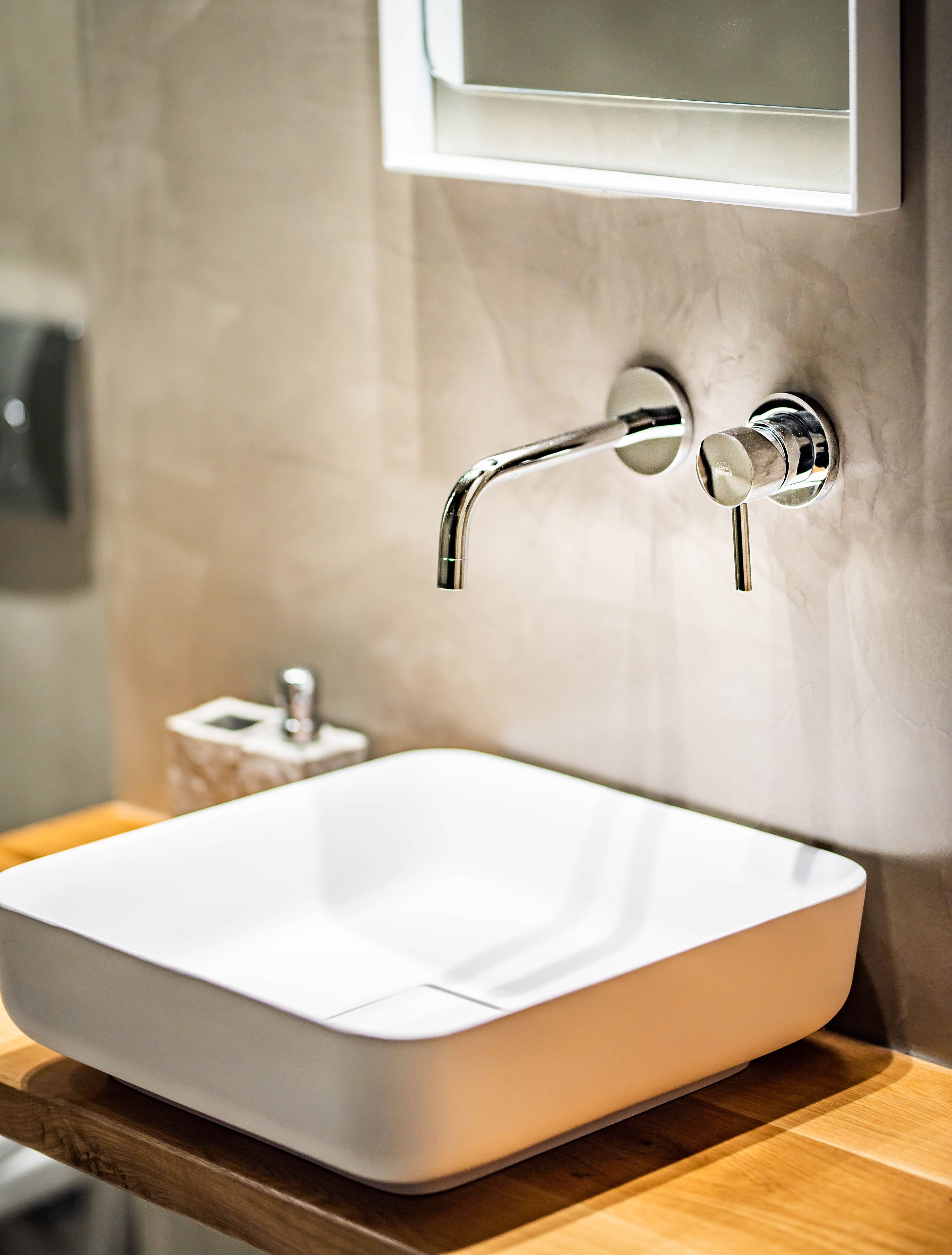 Une salle de bain avec un lavabo rectangulaire blanc, un robinet chromé et un mur en marbre.