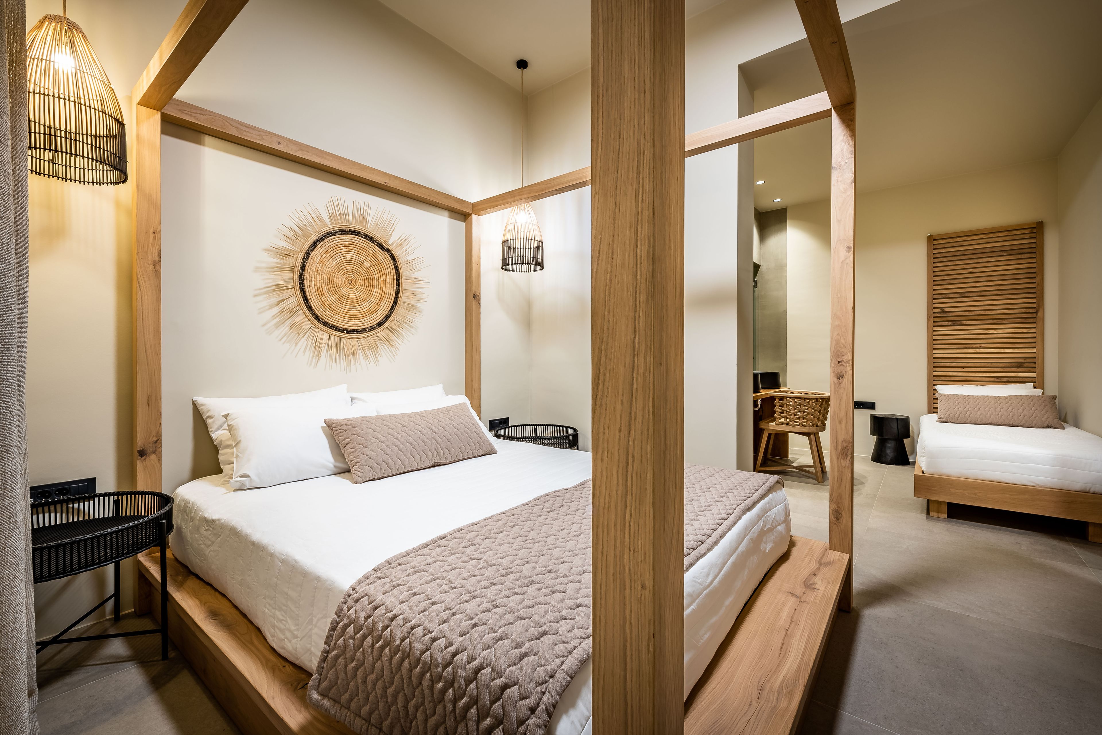 A bedroom with a large bed, a bedside table, a wall-mounted lamp, and a woven wall decoration.