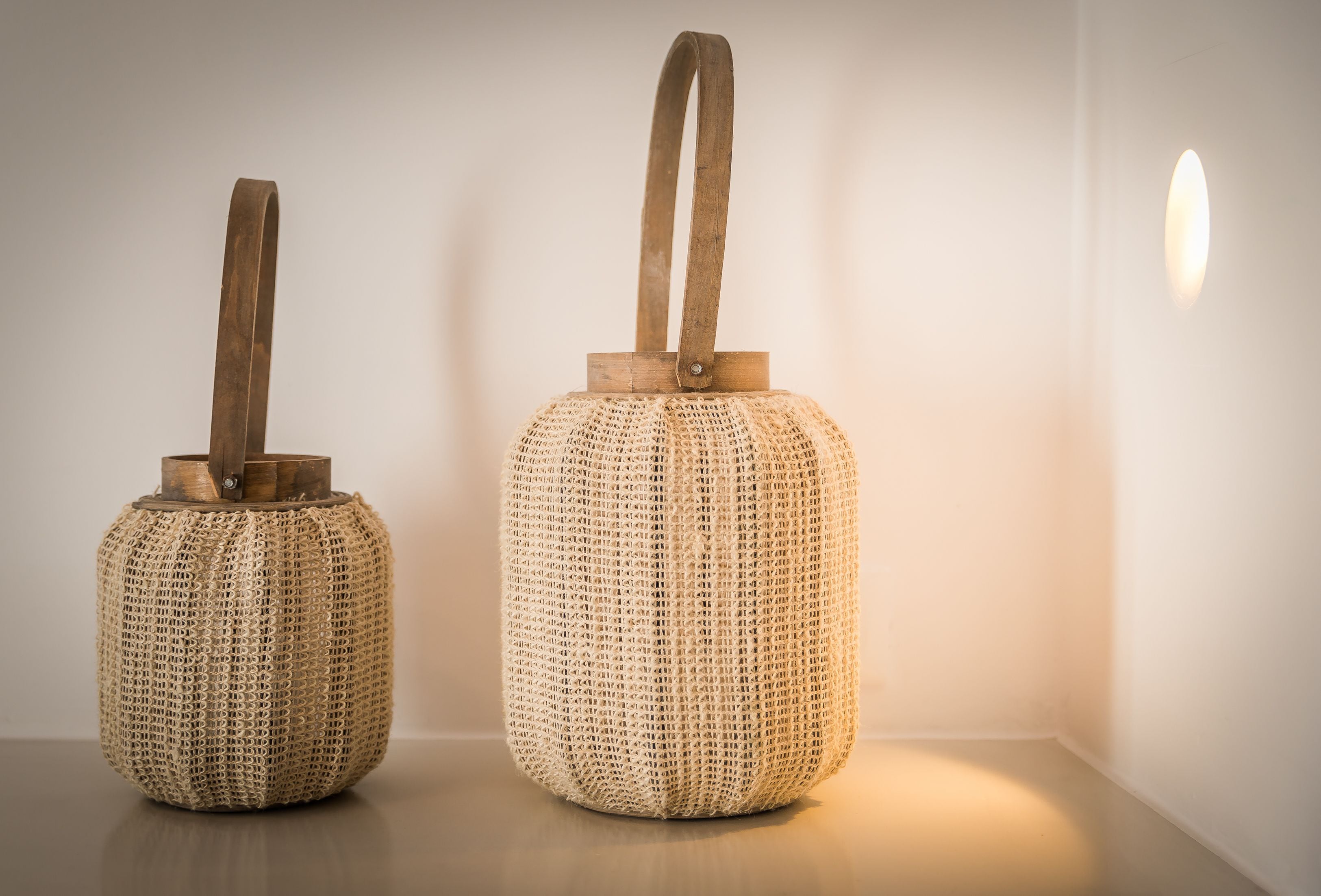 Two woven baskets with handles on a wooden surface against a plain wall.