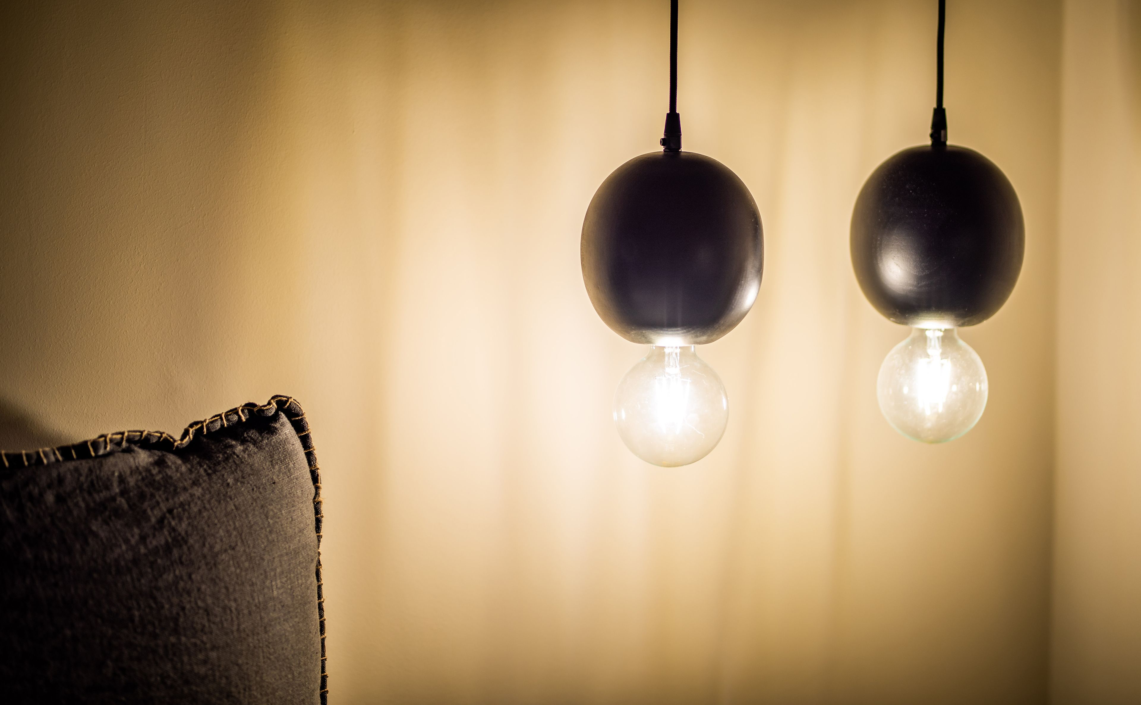 Two hanging spherical light fixtures with exposed bulbs, a textured wall, and a dark-colored pillow.