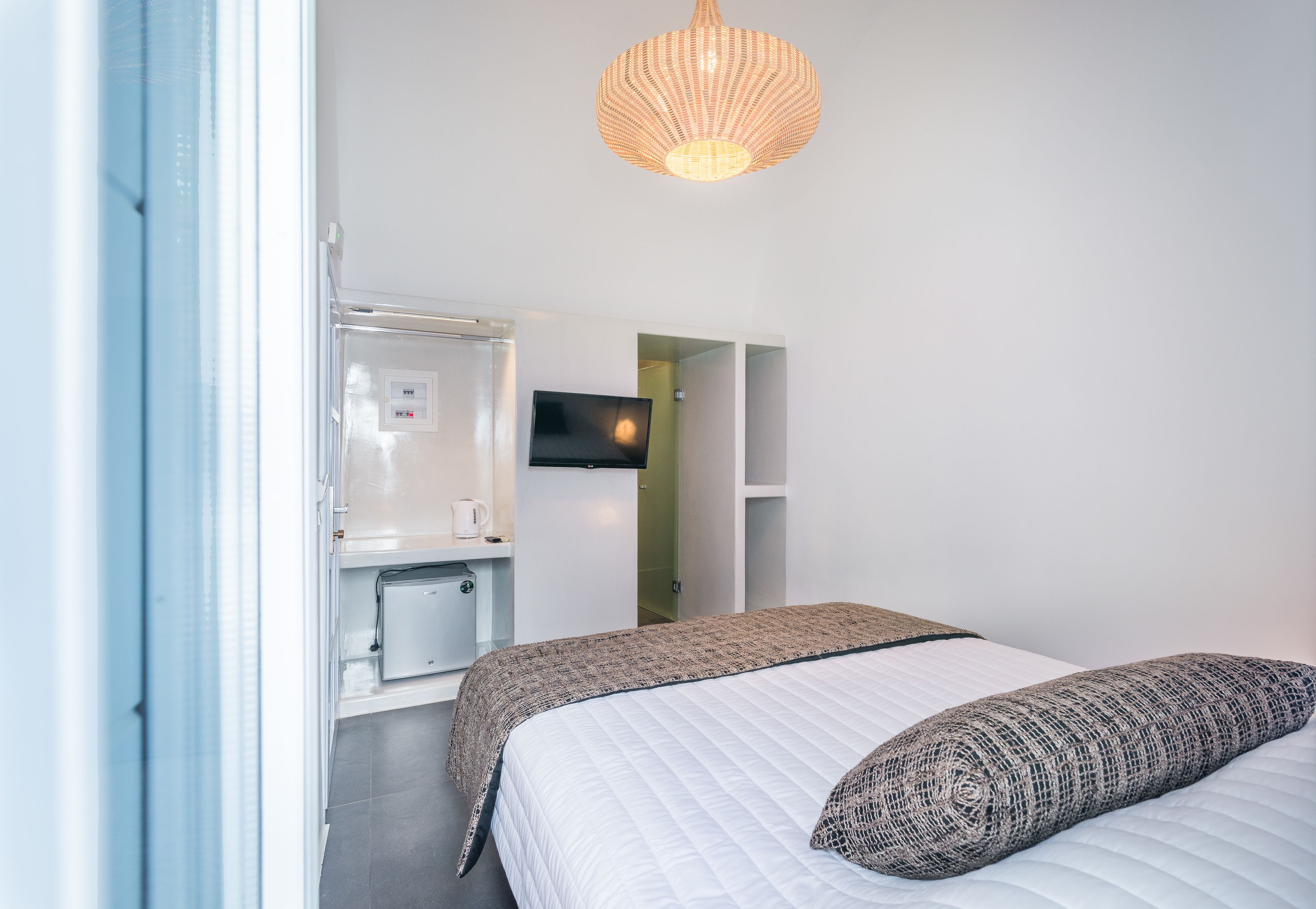 A modern hotel room with a bed, a television, a wardrobe, and a kitchenette.