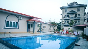 A swimming pool with a tiled deck, a covered seating area, and a multi-story building with balconies. - Hotel Utsab Himalaya (Pokhara)