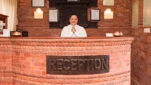 A reception desk with a sign reading "RECEPTION" in a hotel lobby with brick walls and framed certificates. - Hotel Utsab Himalaya (Pokhara)