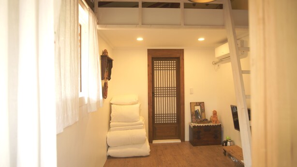 A narrow hallway with a wooden door, a white cushioned bench, and a small table with a decorative item. - Ga In Dang (Jeonju)