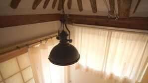A room with a hanging lamp, wooden beams, a window with curtains, and a wall-mounted light switch. - Ga In Dang (Jeonju)