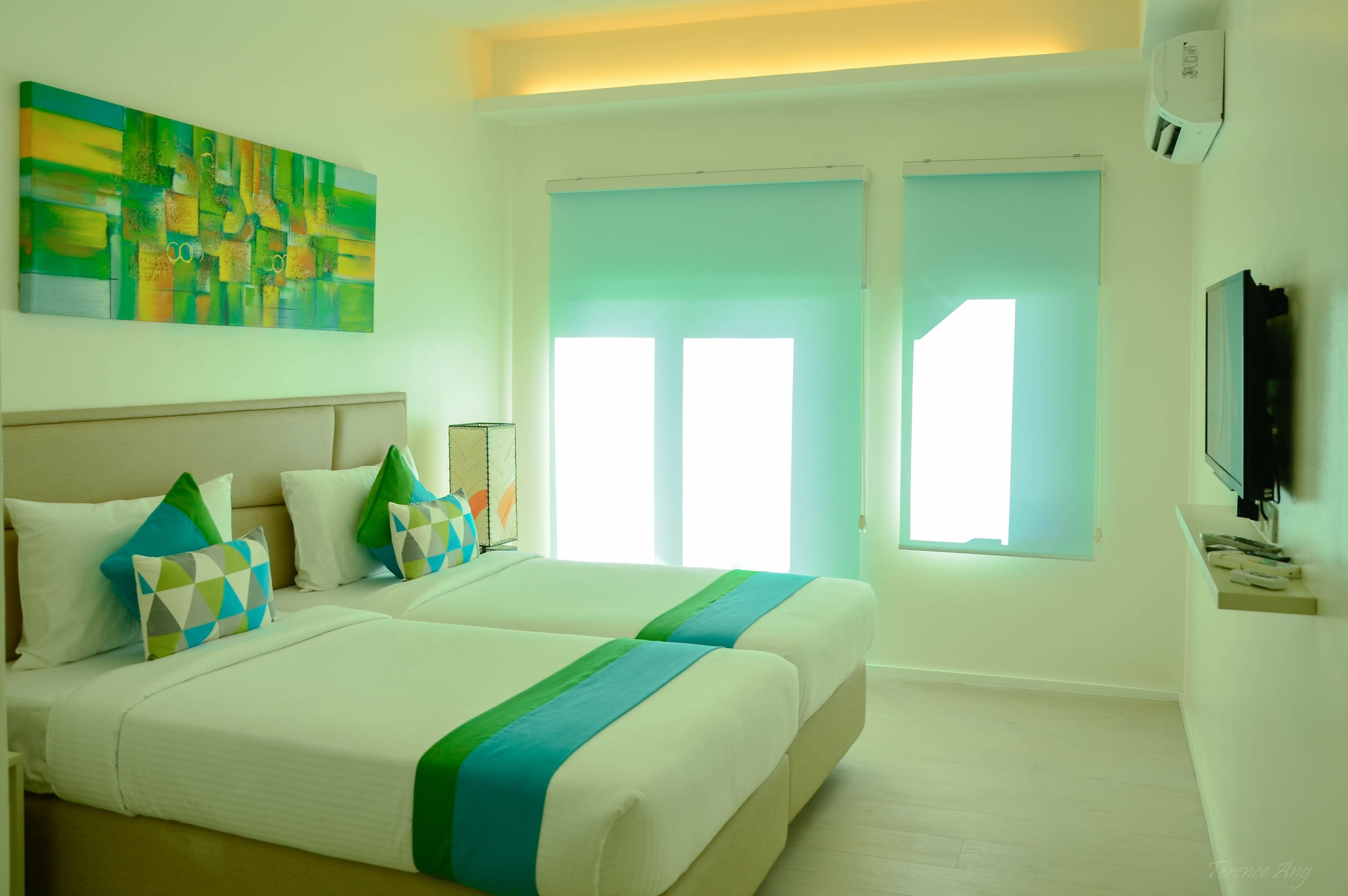 Habitación de hotel con dos camas, un cuadro abstracto grande, un televisor y una puerta corrediza al exterior.