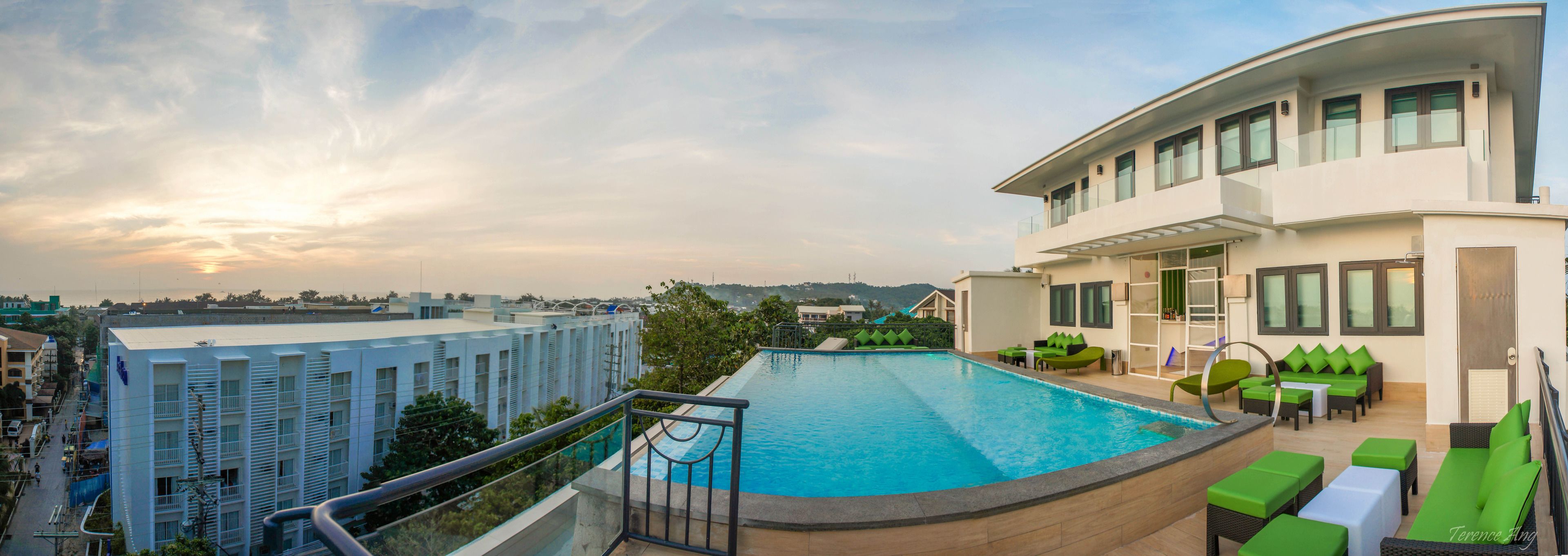 A rooftop pool with a view of the cityscape, a lounge area with green furniture, and a modern building with balconies.
