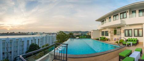 A rooftop pool with a view of the cityscape, a lounge area with green furniture, and a modern building with balconies.