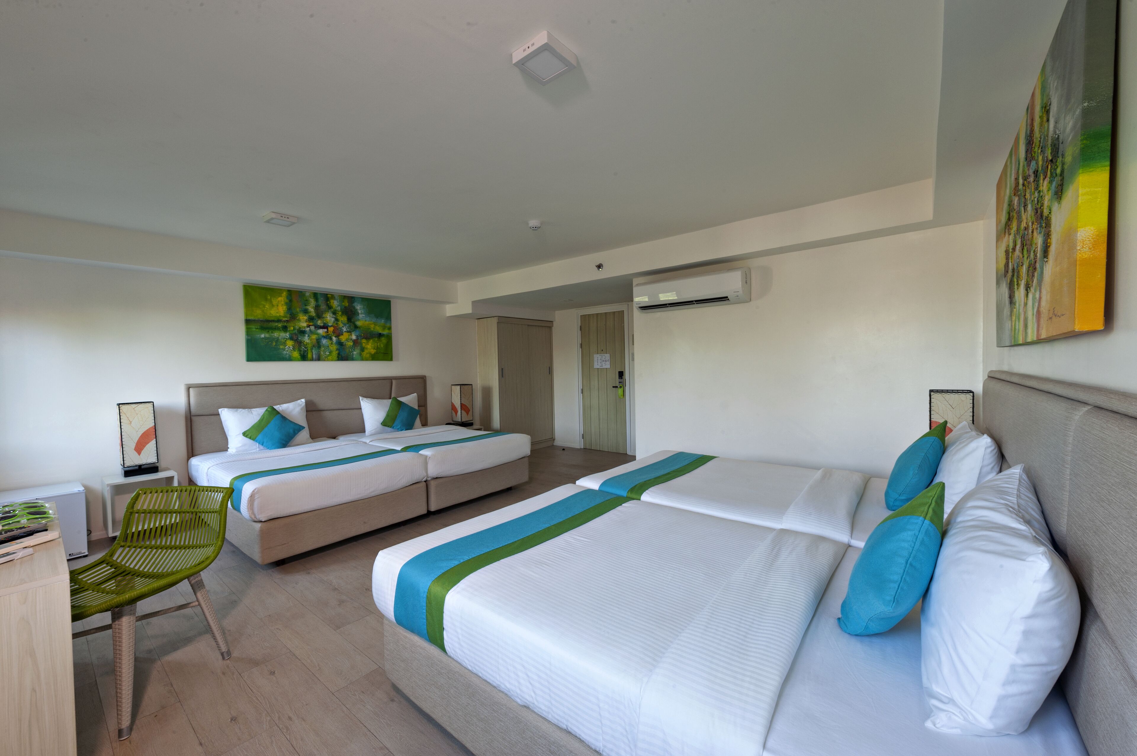 Een hotelkamer met twee bedden, een bureau, een stoel en kunstwerken aan de muur.