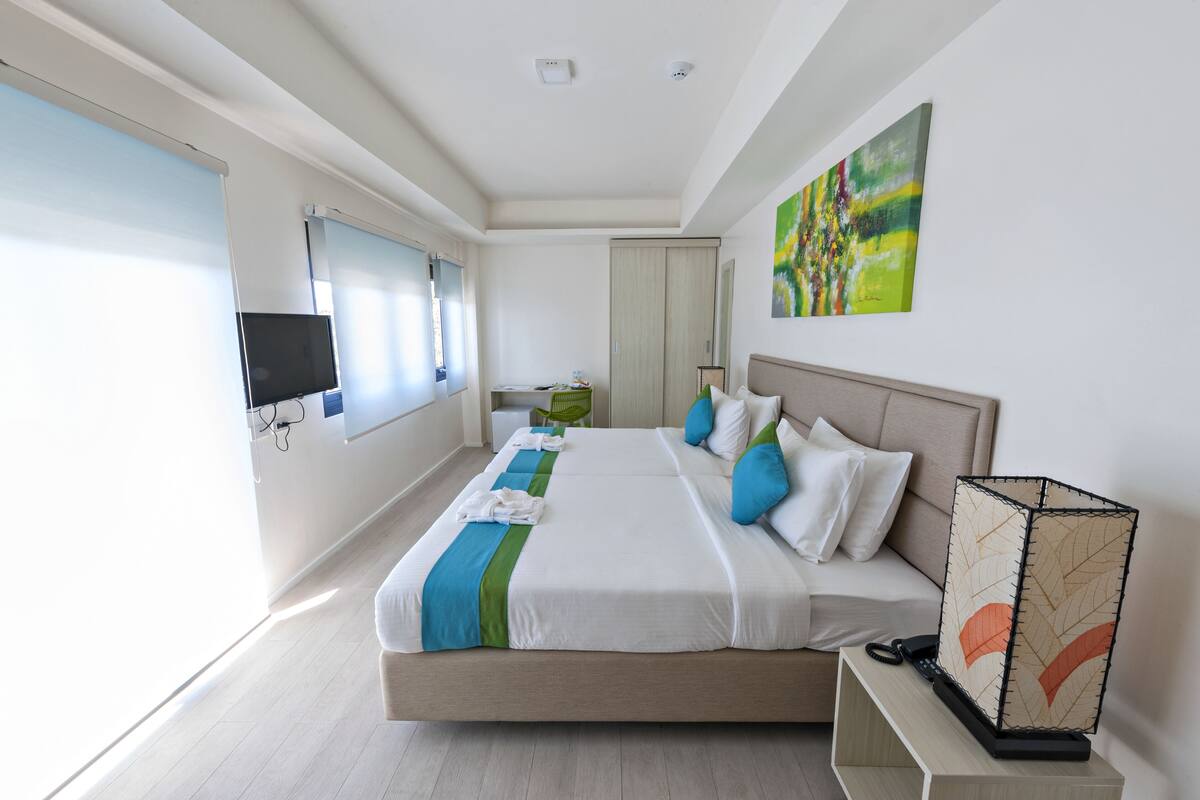 Ein modernes Hotelzimmer mit einem großen Bett, einem Flachbildfernseher, einem Gemälde an der Wand und Blick auf die Stadt.