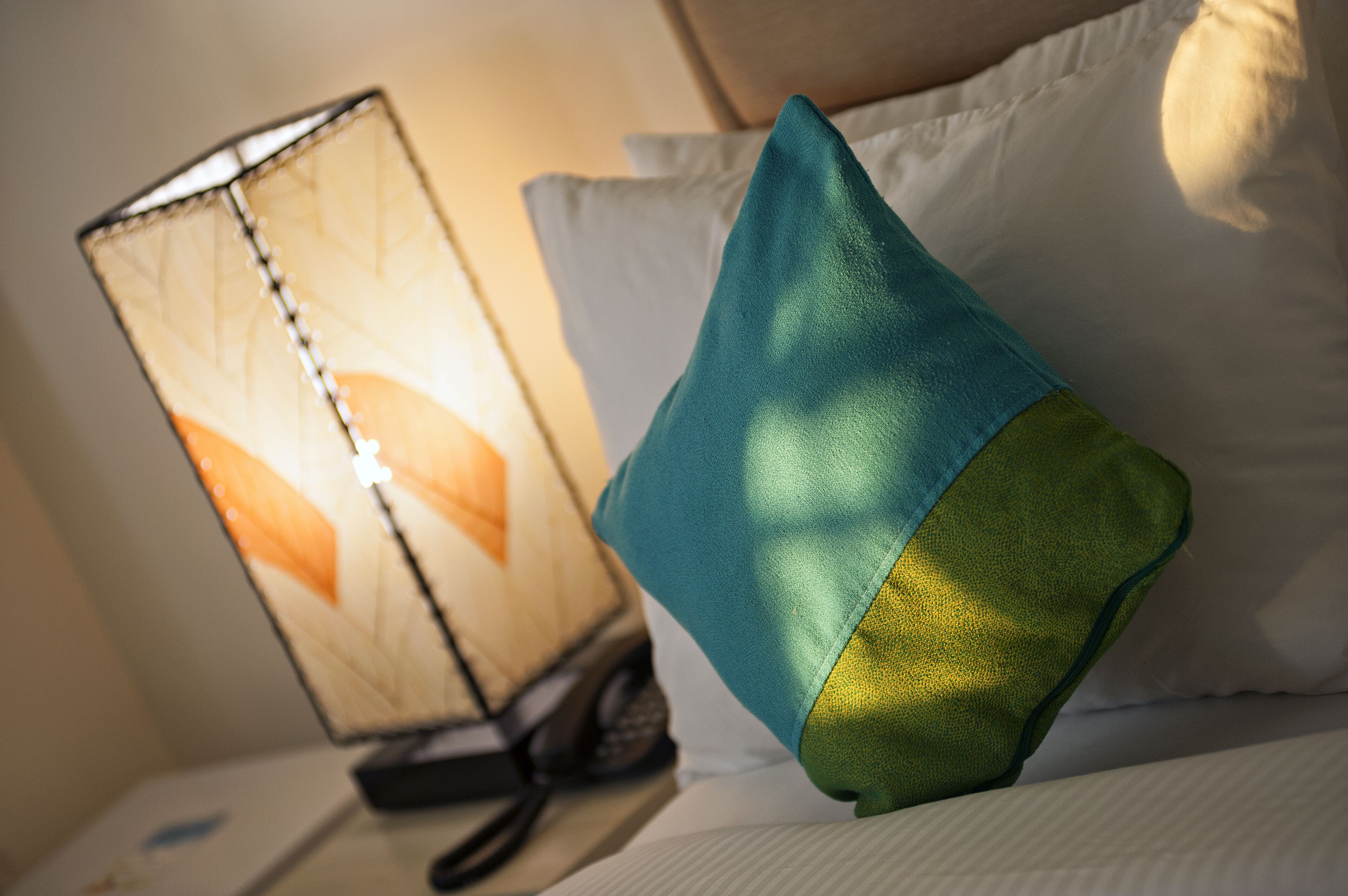 Un letto con un cuscino verde acqua e verde, e una lampada decorata con un motivo a foglia.