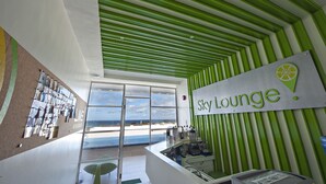 Een moderne lounge met een bordje met de tekst 'Sky Lounge' en uitzicht op het strand door grote ramen.