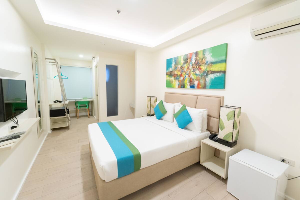 Ein Hotelzimmer mit Bett, Nachttisch, Fernseher, Schreibtisch, Stuhl und Klimaanlage.