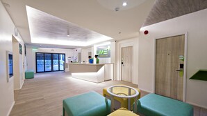 Een moderne hotelentree met een receptiebalie, zithoek en een grote glazen deur.