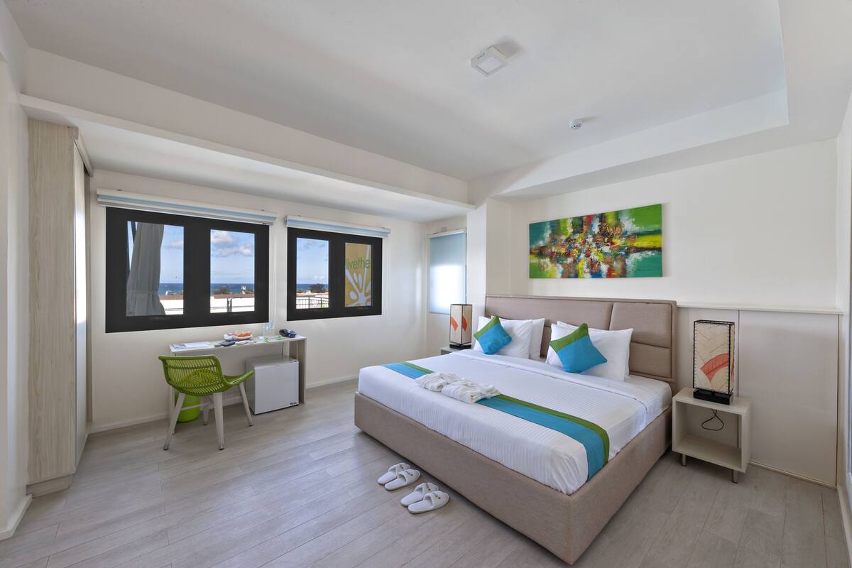 Ein modernes Hotelzimmer mit einem großen Bett, einem Schreibtisch und Meerblick durch die Fenster.