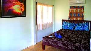 A bedroom with a bed, a window with curtains, an air conditioner, and a tapestry on the wall. - The Boardroom Beach Bungalows (Koh Samui)