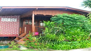 A rustic building with a brick facade, a wooden porch, and a green garden area. - The Boardroom Beach Bungalows (Koh Samui)