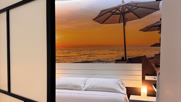 A bedroom with a bed, nightstands, and a view of the ocean at sunset. - Color Suites Alicante (Alicante)