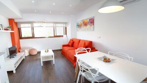 A modern living room with a sofa, a dining table, and a TV. - Color Suites Alicante (Alicante)