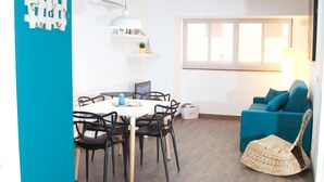 A modern living room with a blue sofa, a dining table with chairs, and a wicker ottoman. - Color Suites Alicante (Alicante)