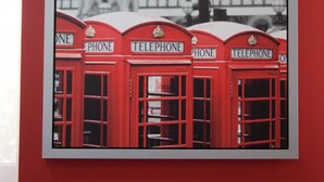 A wall-mounted photograph of red telephone booths with a historic building in the background. - Color Suites Alicante (Alicante)