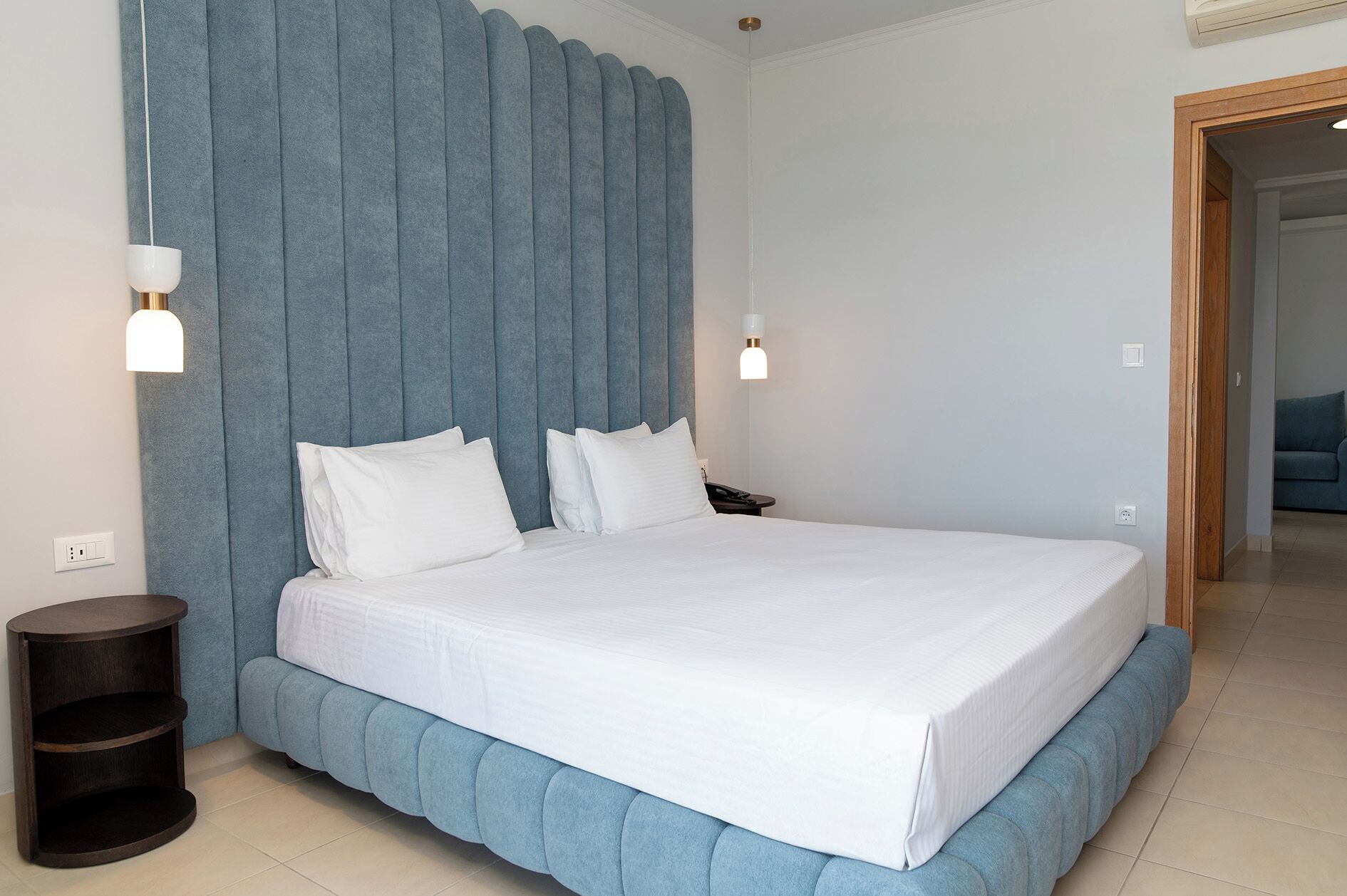 Ein modernes Schlafzimmer mit einem großen Bett, einem blauen Kopfteil, zwei Nachttischlampen und einem dunklen Holznachttisch.