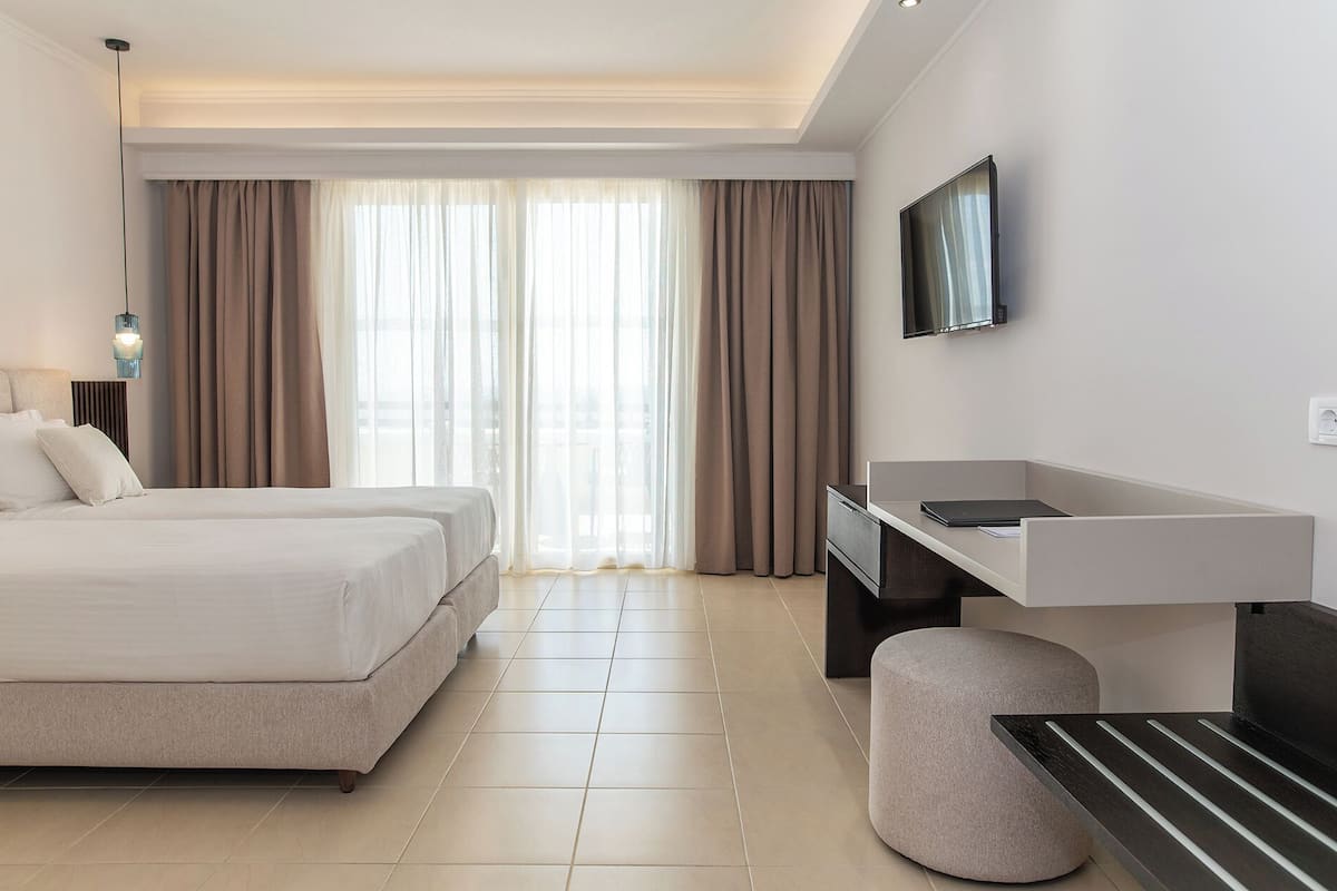 A hotel room with a bed, a desk, a TV, and a window with curtains.