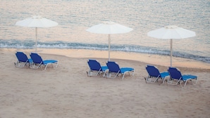 A beach with rows of blue lounge chairs and white umbrellas, facing the ocean. - Grand Blue Beach Hotel (Kos)