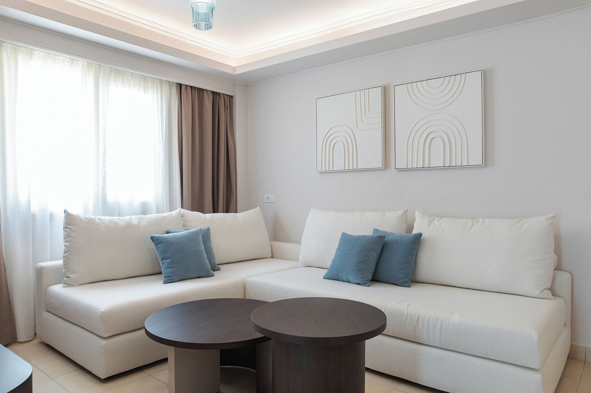Ein modernes Wohnzimmer mit einem beigefarbenen Ecksofa, zwei runden Couchtischen und abstrakter Wandkunst.